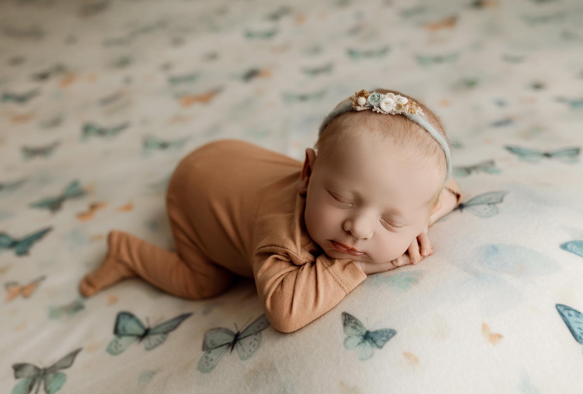 Newborn sleeping on soft cream fabric with sage, teal, and peach butterfly prints, wearing a matching floral headband.
