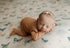 Newborn sleeping on soft cream fabric with sage, teal, and peach butterfly prints, wearing a matching floral headband.