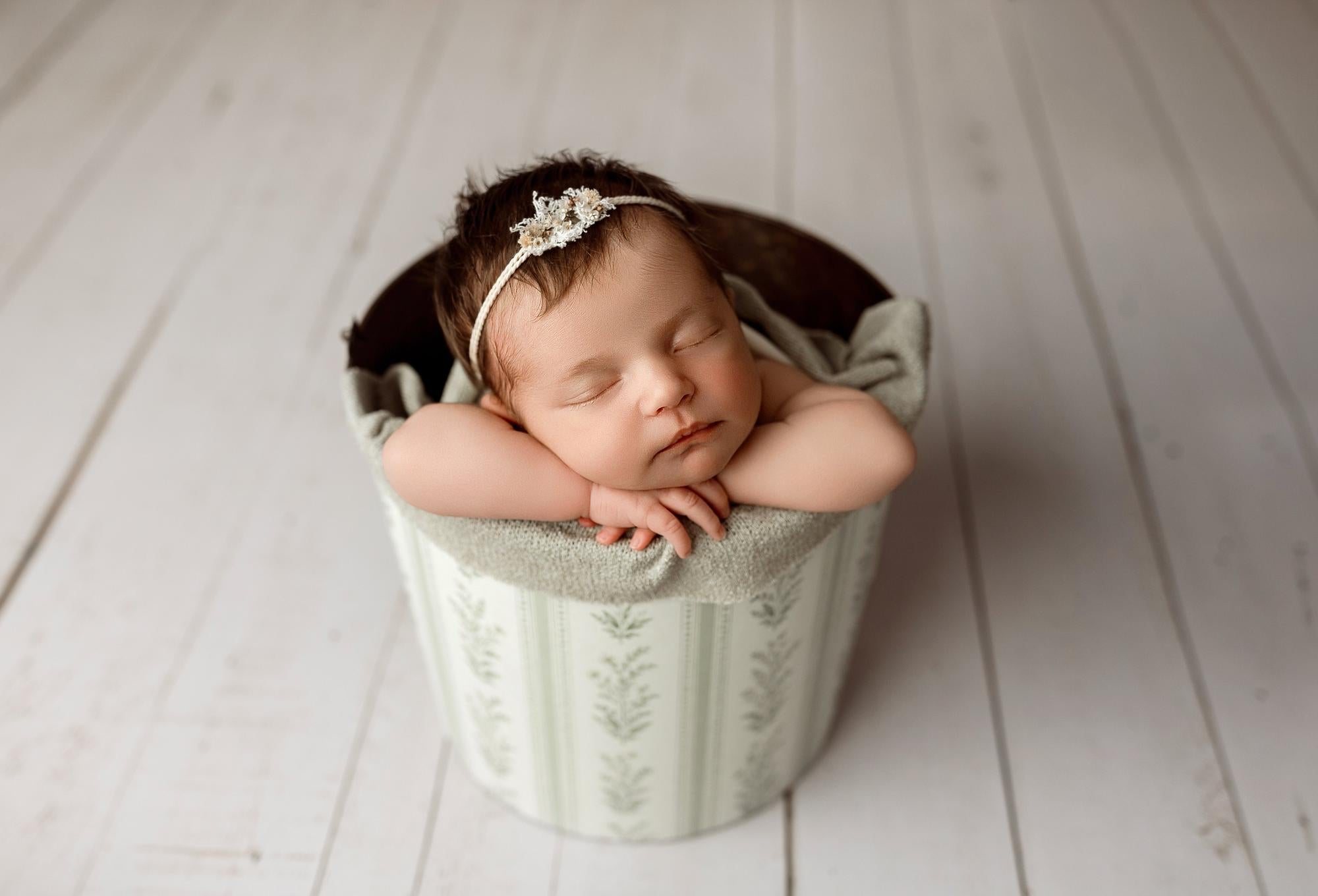 Newborn baby sleeping in a bucket wrapped in a textured, sage gray Nest fabric with organic, earthy styling.