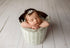 Newborn baby sleeping in a bucket wrapped in a textured, sage gray Nest fabric with organic, earthy styling.