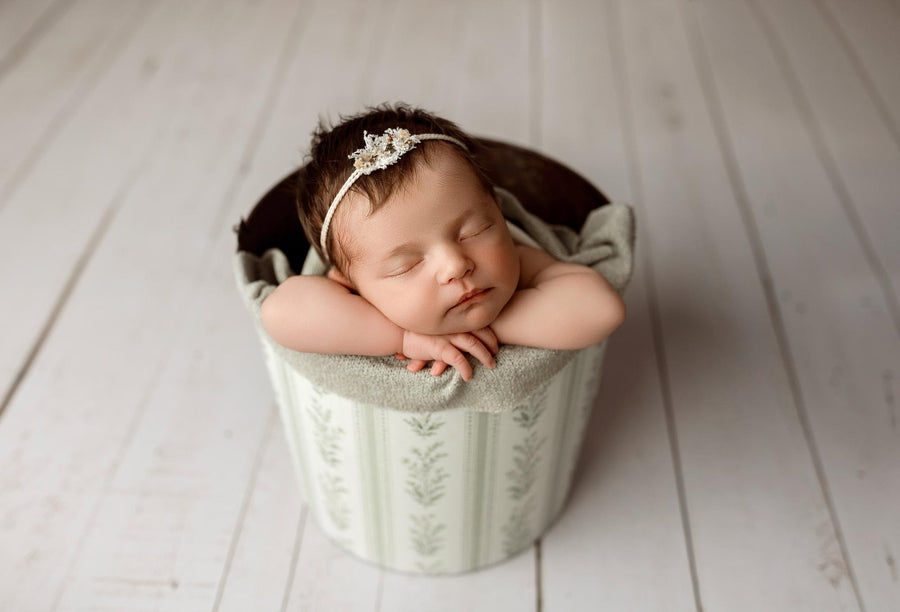Newborn baby sleeping in a bucket wrapped in a textured, sage gray Nest fabric with organic, earthy styling.