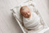 Newborn baby swaddled in soft, ivory open-knit fabric, resting in a white wooden prop bed.