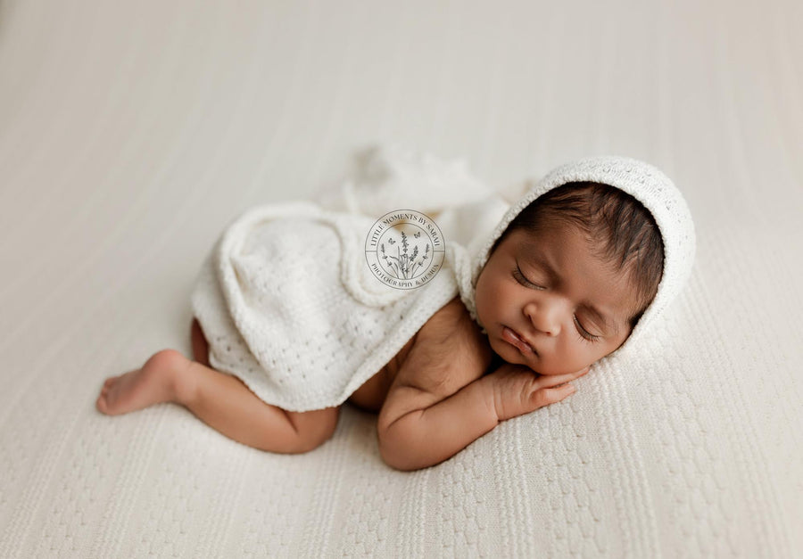 Newborn baby draped in a textured cream knit wrap posed on a coordinating newborn photography posing fabric.