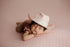 Newborn baby sleeping on a textured baby pink posing fabric, wearing a matching ruffle wrap and a light pink cowboy hat.