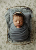 Newborn baby wrapped in dusty blue fabric on a Hayden Floral posing cloth with sage green and cream wildflowers.
