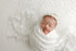Sleeping newborn baby wrapped in ivory fabric with Minimalist lace layer and coordinating delicate ivory floral headband.