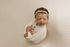 Newborn wrapped in a creamy peach-toned ribbed knit fabric with a matching headband on a textured posing backdrop.