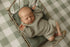 Newborn sleeping on a soft moss green velvet pillow inside a vintage metal bed frame.