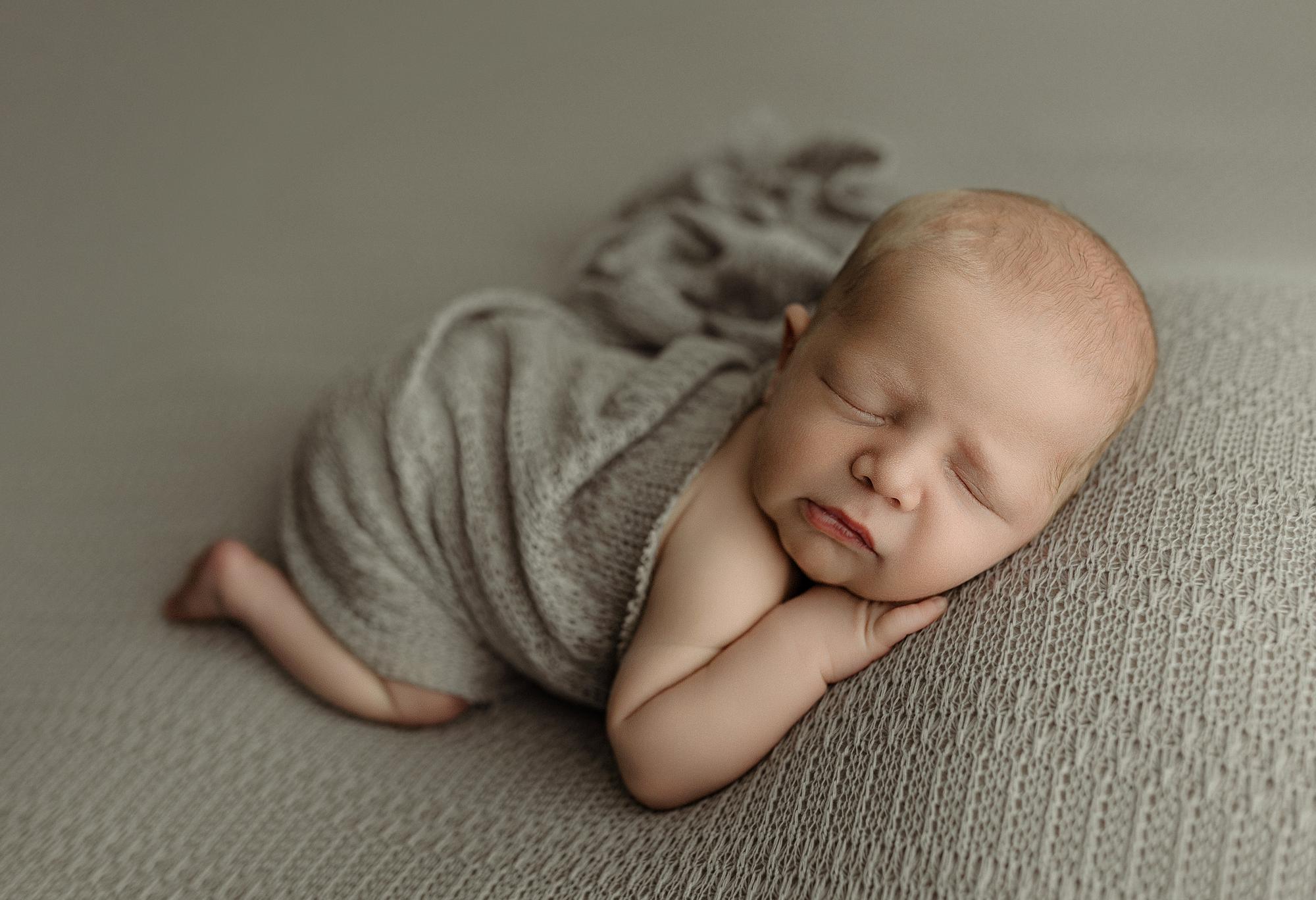 Newborn sleeping on a textured, storm gray knit fabric drop and matching wrap.