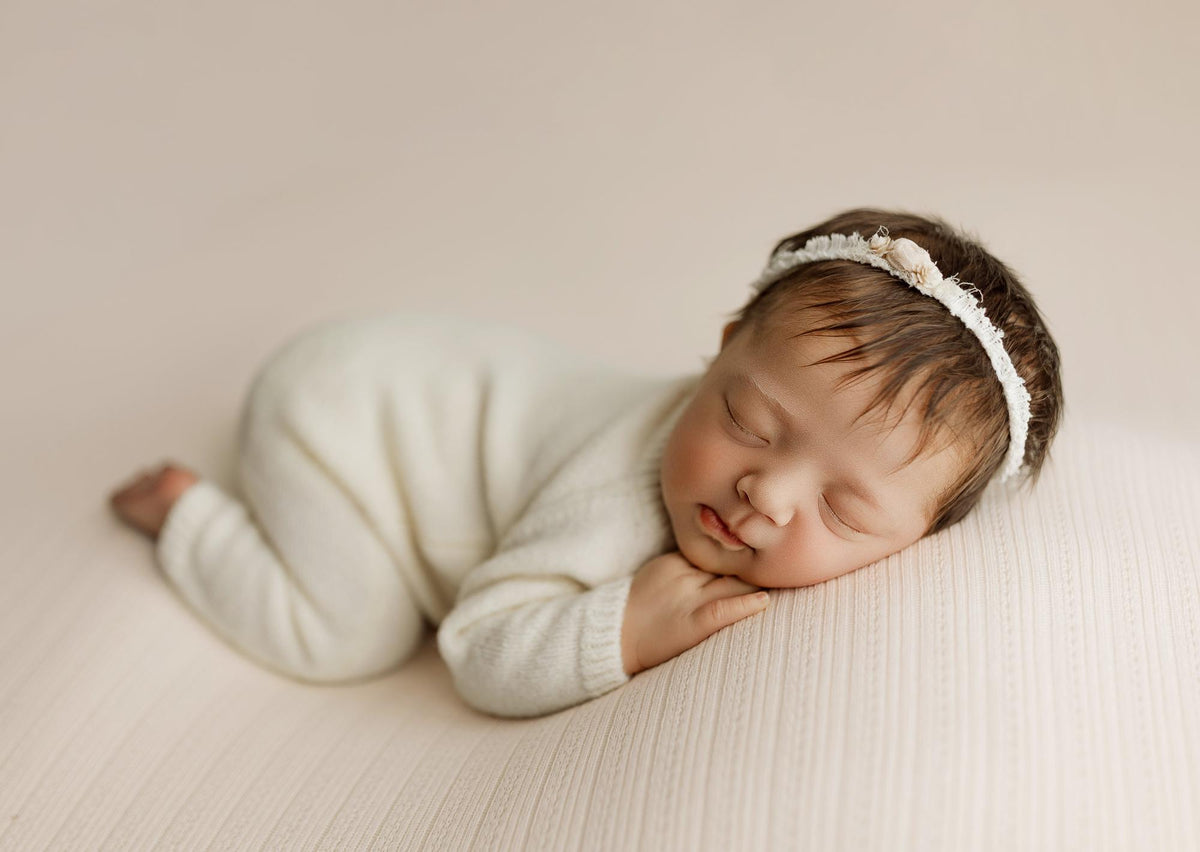Newborn sleeping on a creamy ivory ribbed knit drop and wrap with subtle peach undertones and delicate texture.