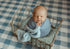 Newborn baby wrapped in a blue Tatter Smurf open-knit fabric, resting in a vintage metal bed prop.