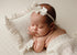 Newborn sleeping on a textured off-white Veda posing fabric and matching ruffled pillow with a delicate bow headband.