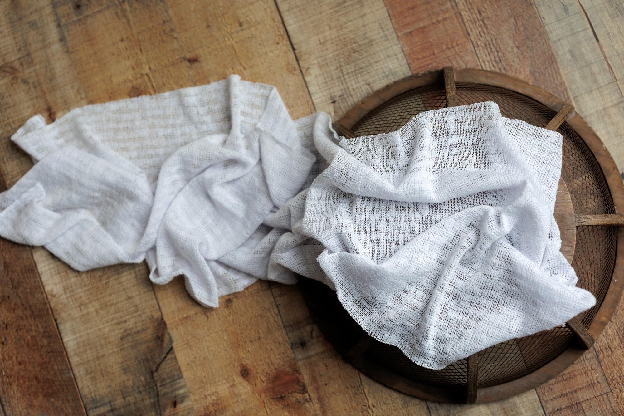 Lightweight, cool-toned ivory newborn photography wrap with a soft, airy textured knit draped over a rustic wooden prop.