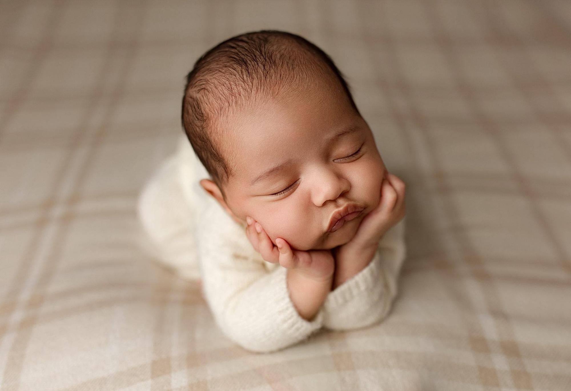 Newborn resting on a soft, neutral plaid posing fabric with a timeless vintage check pattern.