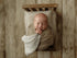 Newborn baby sleeping in a miniature wooden bed with taupe and ivory check bedding and a matching pillowcase.