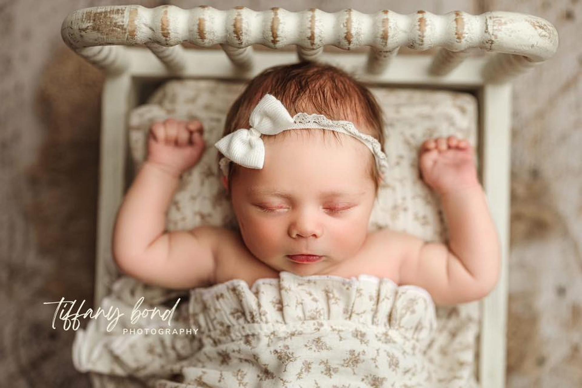 Newborn sleeping on Flowertown floral sheets with a matching ruffle wrap and white bow headband in a vintage bed.