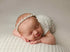 Newborn sleeping on a textured, off-white Veda knit posing fabric with a matching wrap and delicate lace headband.