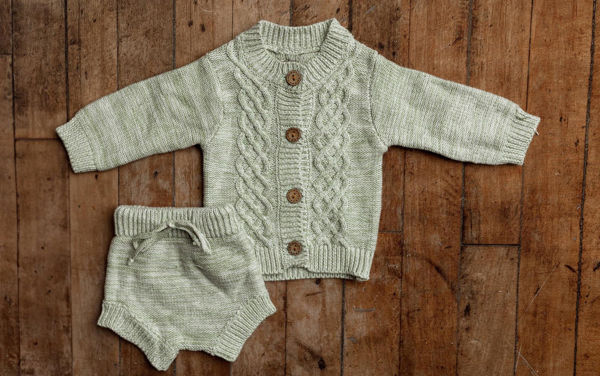 Sage green cable knit newborn photography outfit with wooden button cardigan and matching knit bloomers, a two-piece baby boy outfit for newborn photo sessions.