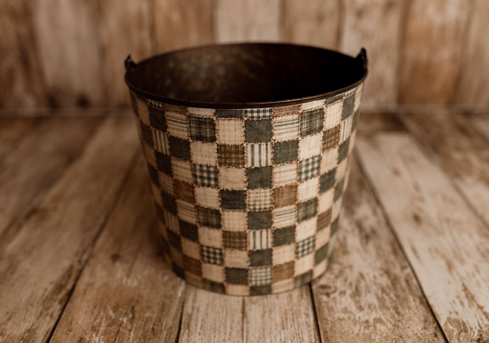 Attic Treasures removable newborn photography bucket cover displayed on a rustic metal posing bucket, featuring olive green and cream vintage quilt patchwork.