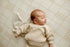 Close-up of sleeping newborn wearing a textured oatmeal knit sweater on Grandpa's Twin beige plaid posing fabric with a coordinating mini blankie.