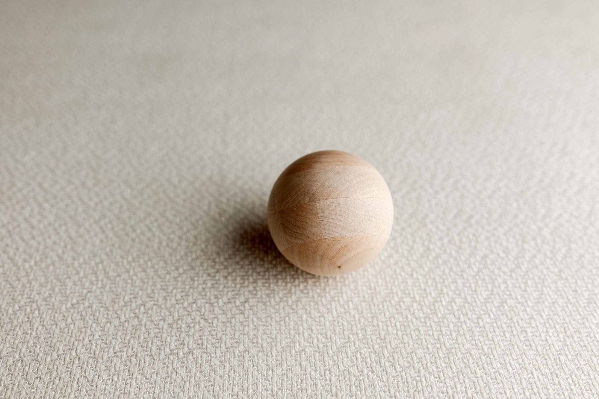 Warm ivory textured knit fabric with subtle shimmer, featuring a smooth wooden sphere prop for newborn photography.
