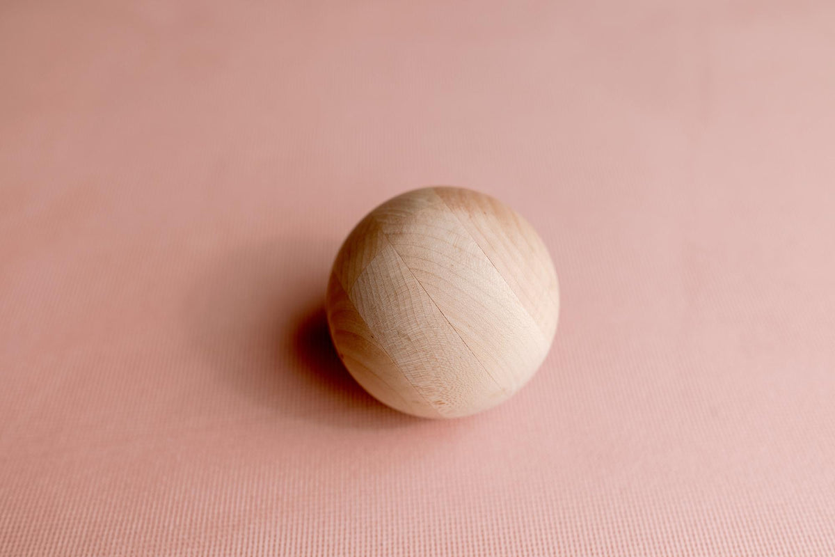 Smooth wooden ball resting on a soft, blush pink textured knit newborn photography backdrop.