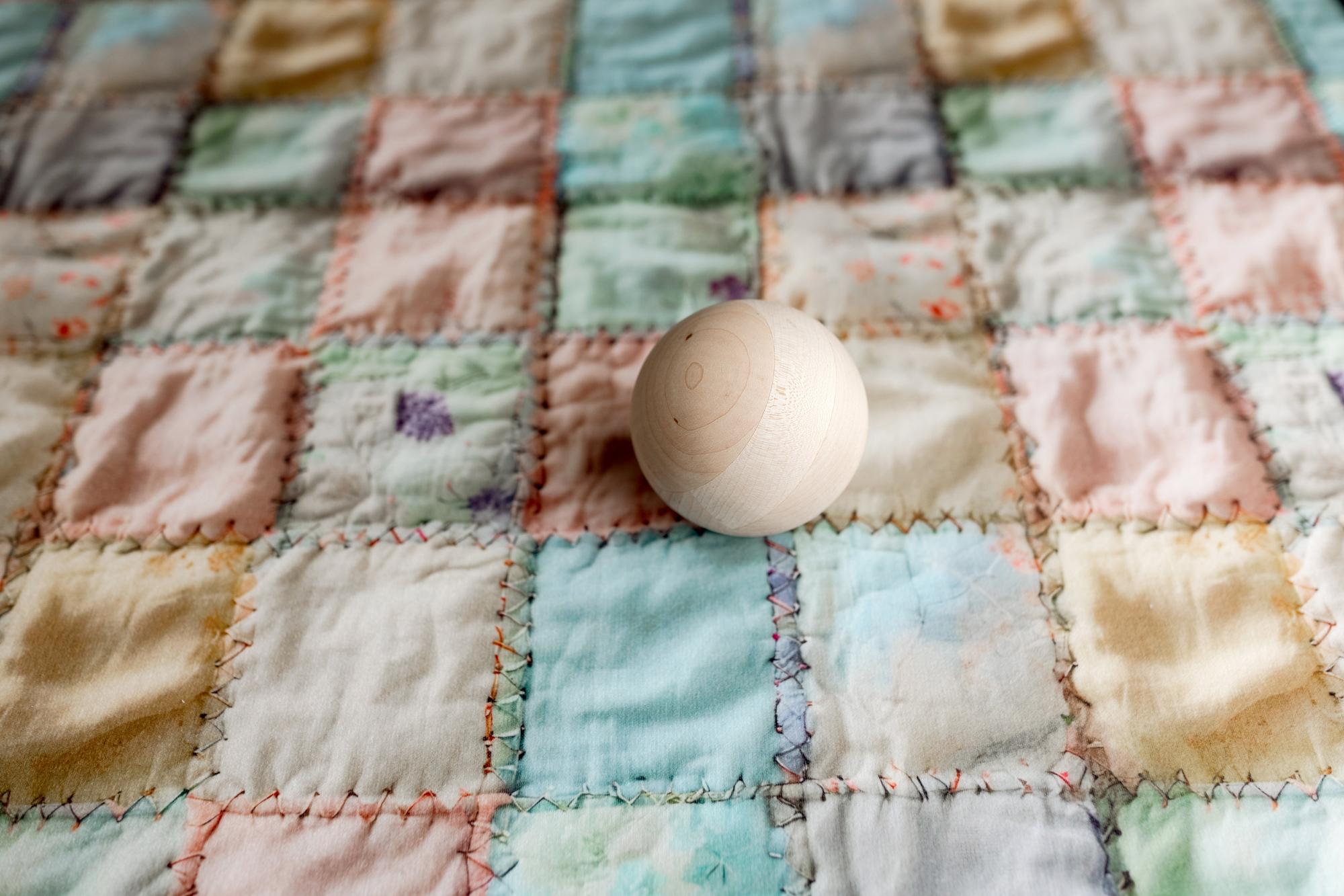 Pastel patchwork quilt posing fabric with realistic stitching and a smooth wooden sphere prop.