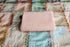 Folded carnation pink stretchy knit newborn posing wrap resting on a pastel patchwork quilt.