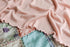 Soft carnation pink stretchy knit newborn photography wrap with ruffled edges draped over a pastel patchwork quilt.
