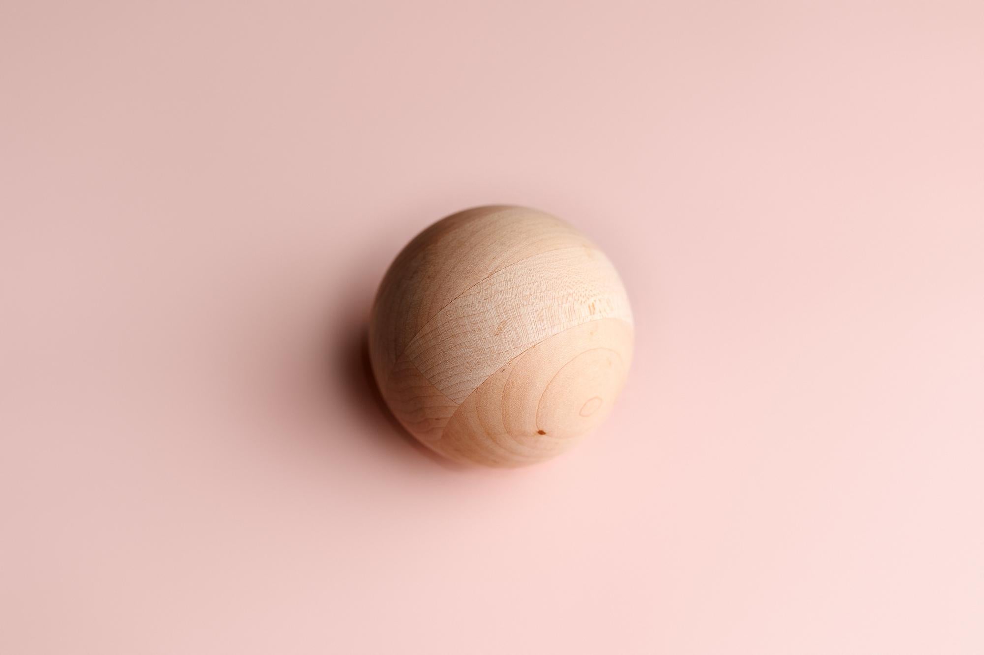 Smooth wooden sphere centered on a soft, blush pink fabric background for newborn photography.
