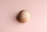 Smooth wooden sphere centered on a soft, blush pink fabric background for newborn photography.