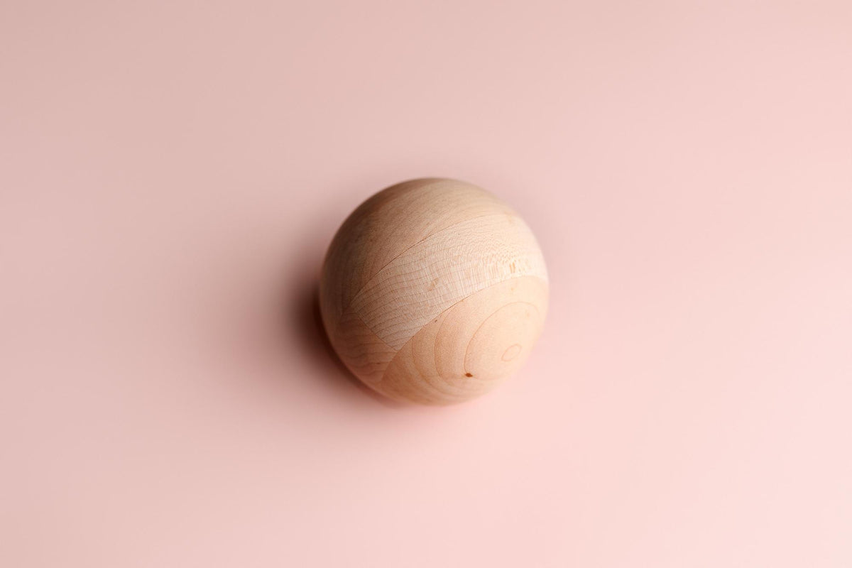 Smooth wooden sphere centered on a soft, blush pink fabric background for newborn photography.