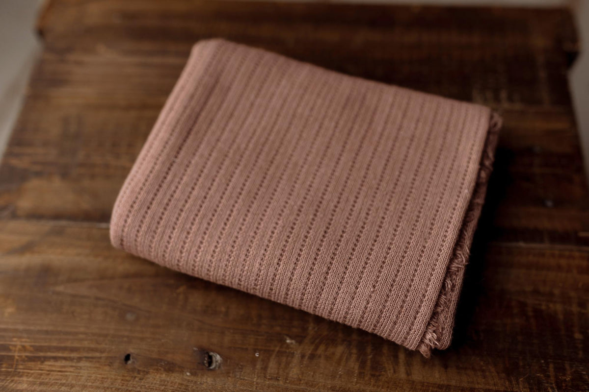 Folded brown-toned purple newborn photography wrap in a lightweight, textured stretch knit fabric.