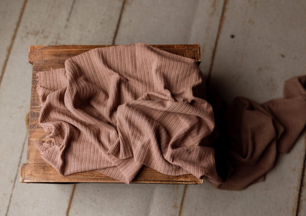 Soft brown-toned purple newborn photography wrap in a lightweight, textured stretch knit fabric draped over a wooden crate.