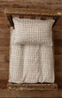Newborn bed sheet and pillowcase in a taupe and ivory woven check pattern on a rustic wooden photography prop bed.