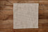 A square beige and brown gingham checkered newborn photography mini blanket laid flat on a rustic wooden plank surface.