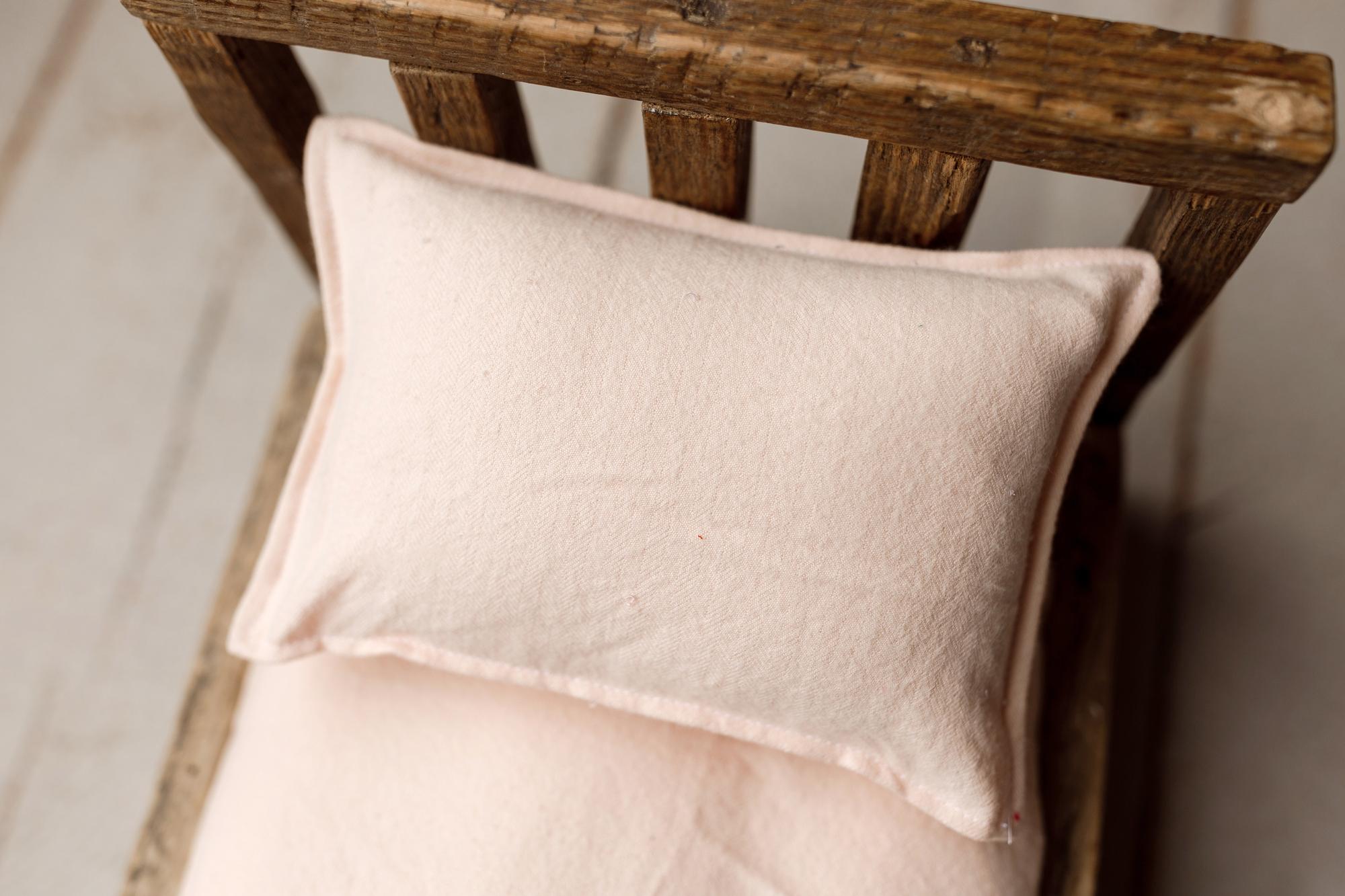 Soft peachy pink linen pillowcase and sheet set for newborn photography props, displayed on a rustic wooden mini bed.