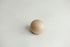 A small, smooth, spherical wooden bead or knob in a light natural wood finish, resting on a textured white newborn posing fabric.