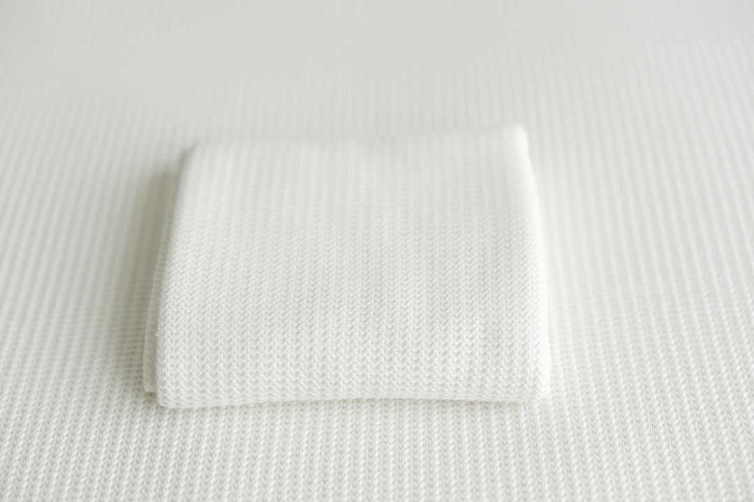 A folded white knit newborn photography wrap on a coordinating posing fabric.