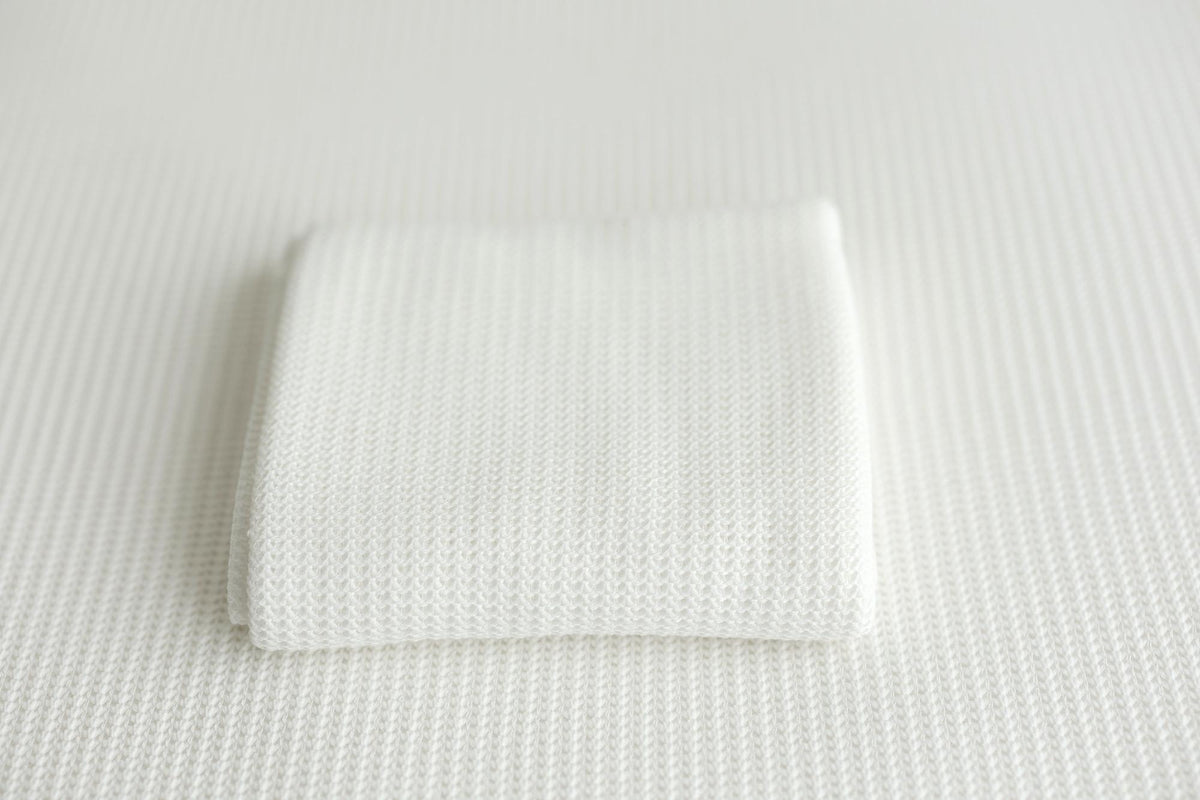A folded white knit newborn photography wrap on a coordinating posing fabric.