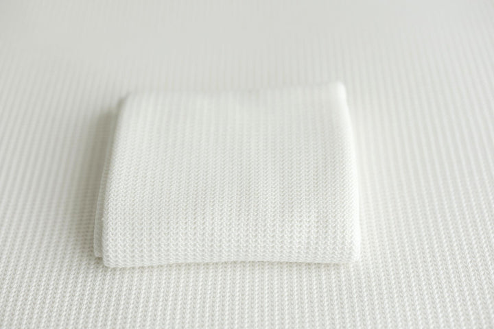 A folded white knit newborn photography wrap on a coordinating posing fabric.