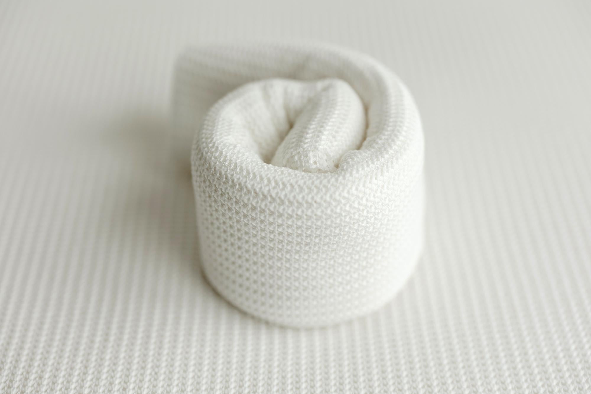 A rolled-up white textured knit fabric wrap for newborn photography props.