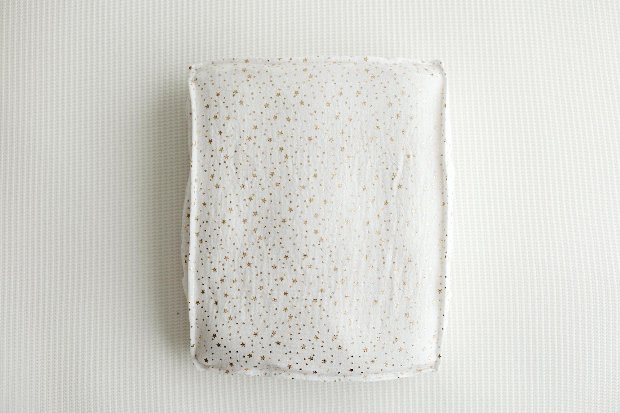 A rectangular ceramic plate with a white glaze and scattered gold speckles, photographed from directly above on a textured white background.