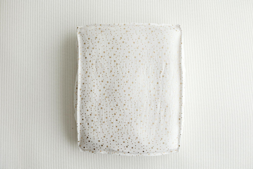 A rectangular ceramic plate with a white glaze and scattered gold speckles, photographed from directly above on a textured white background.