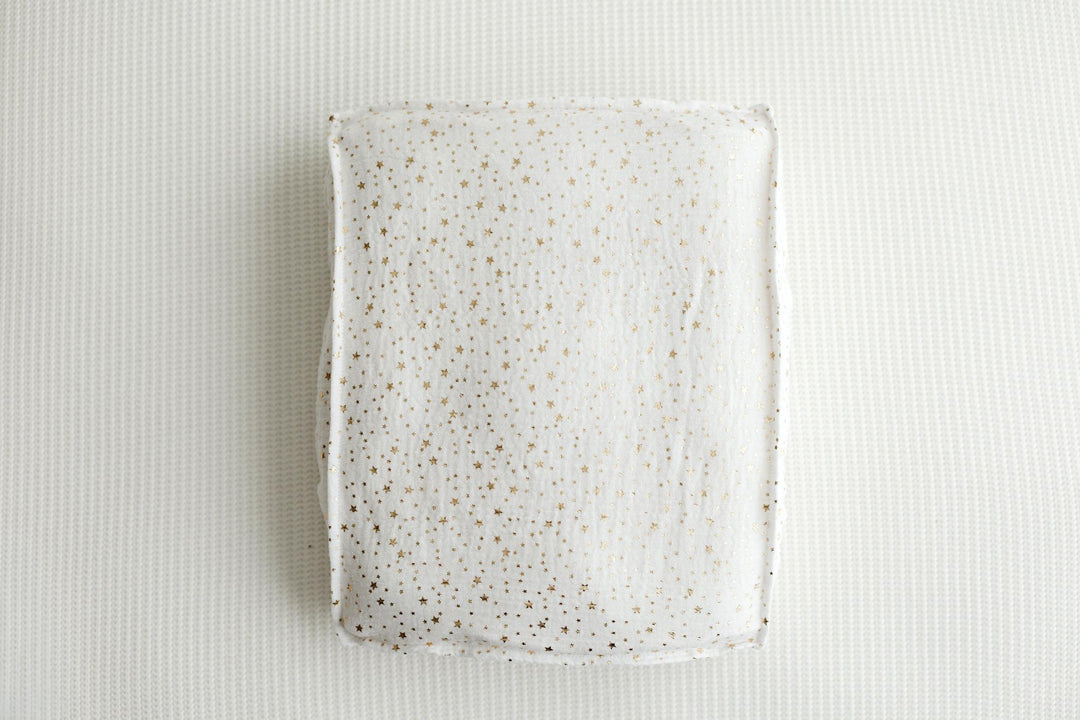 A rectangular ceramic plate with a white glaze and scattered gold speckles, photographed from directly above on a textured white background.