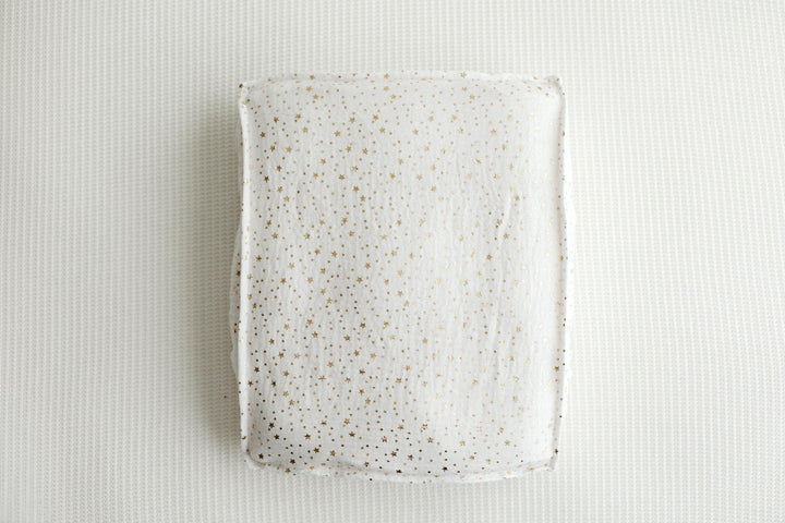 A rectangular ceramic plate with a white glaze and scattered gold speckles, photographed from directly above on a textured white background.