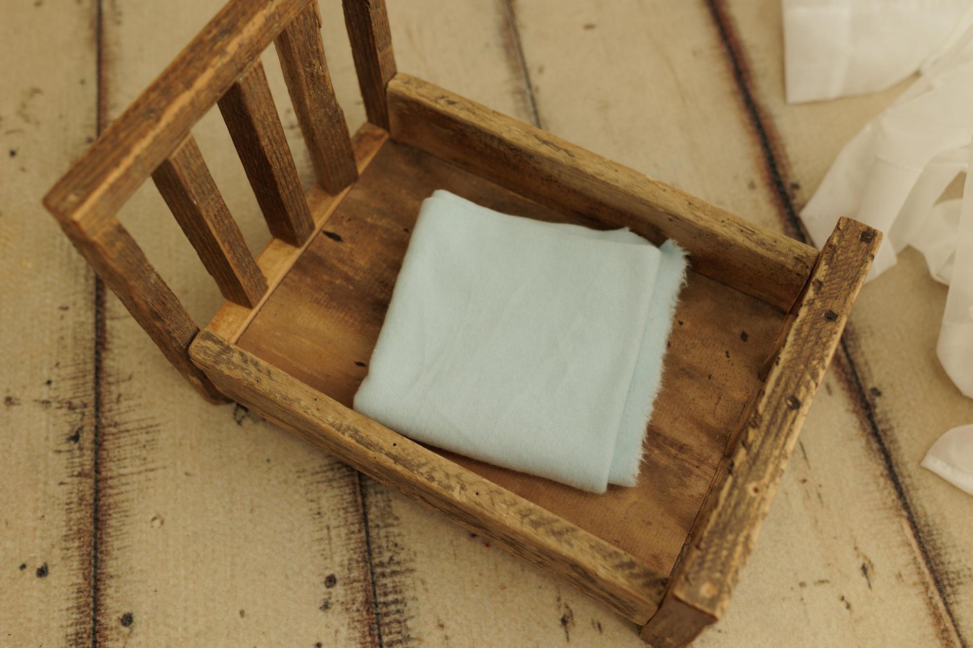 Soft, stretchy light blue fabric folded inside a rustic wooden newborn photography bed prop.
