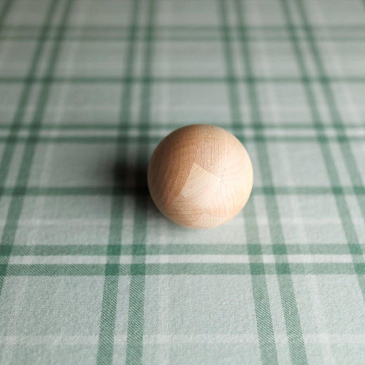 Smooth wooden sphere resting on sage green and cream plaid fabric for newborn photography.