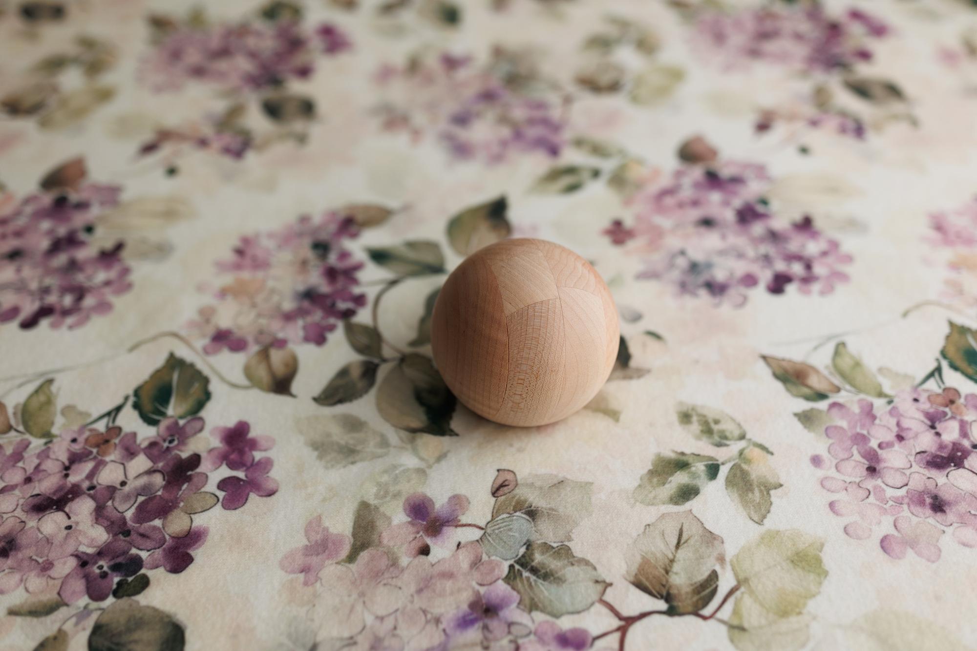 Witney floral posing fabric with watercolor mauve and purple flowers on a creamy neutral base, featuring a wooden sphere.