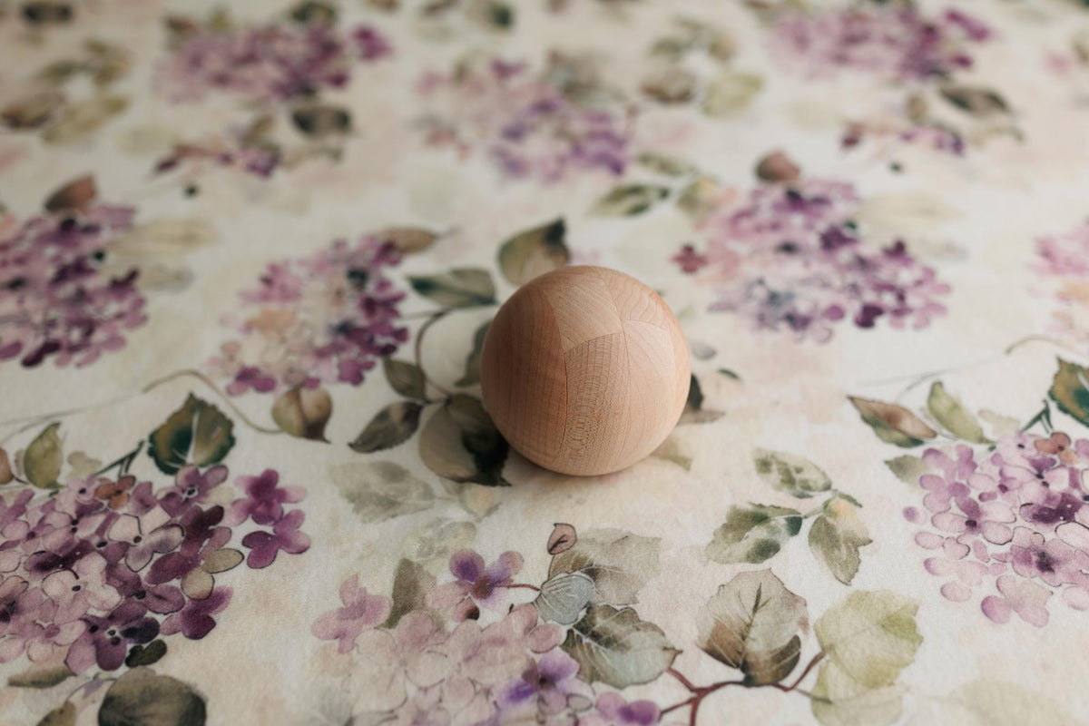 Witney floral posing fabric with watercolor mauve and purple flowers on a creamy neutral base, featuring a wooden sphere.
